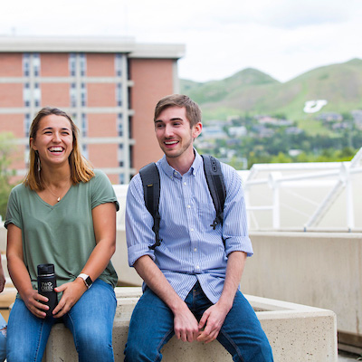 Two students smiling at the camera with the U on the mountainside